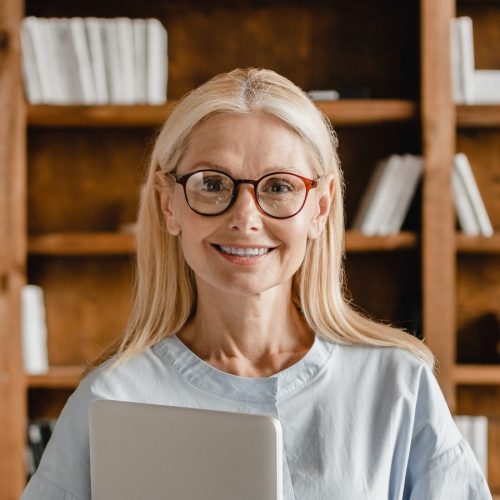 businesswoman-teacher-boss-freelancer-holding-laptop-looking-at-camera-in-glasses-in-office-library-e1656644395390.jpg